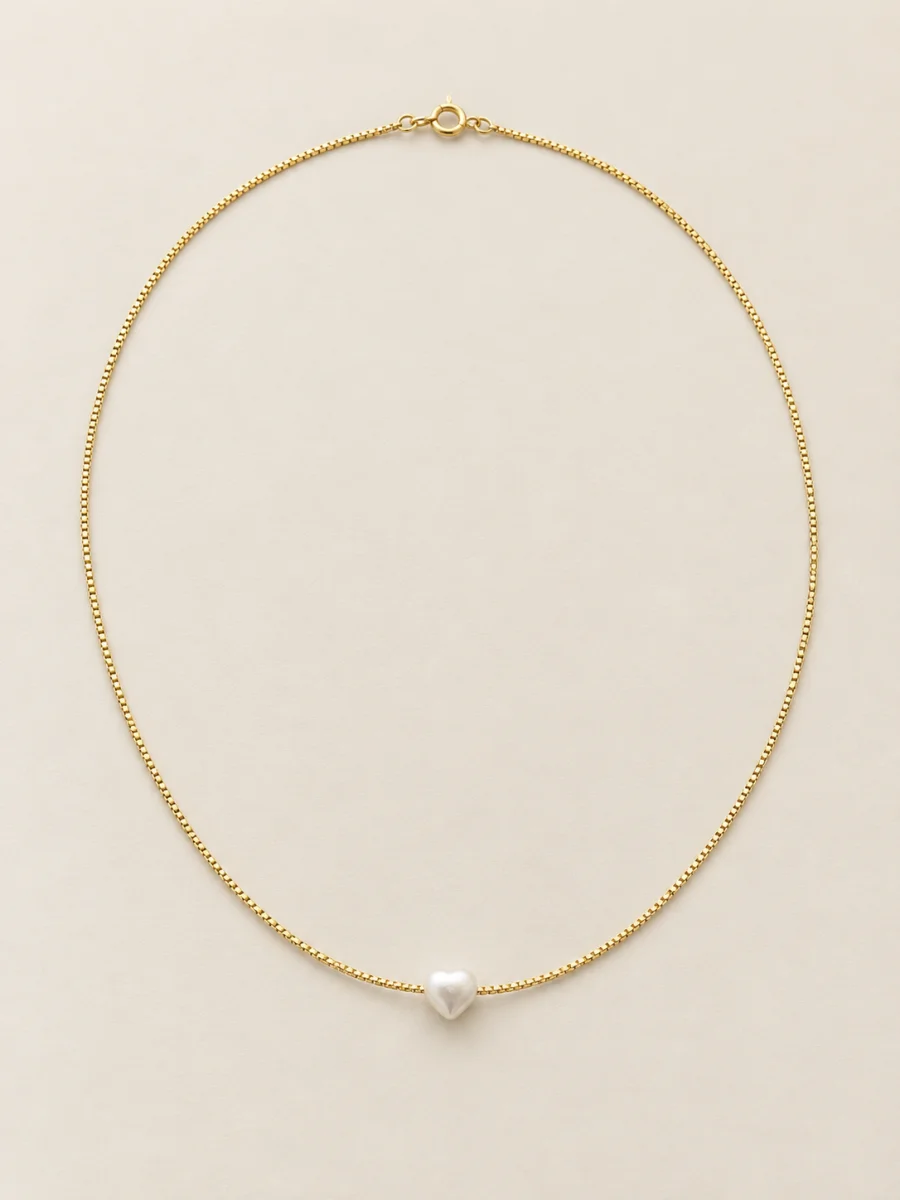 Colar dourado com pérola em coração sobre fundo bege
