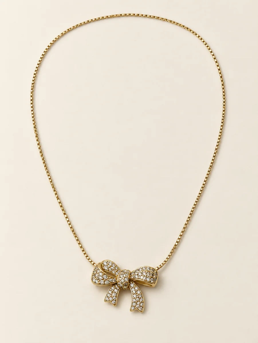 Colar dourado com laço cravejado sobre fundo bege