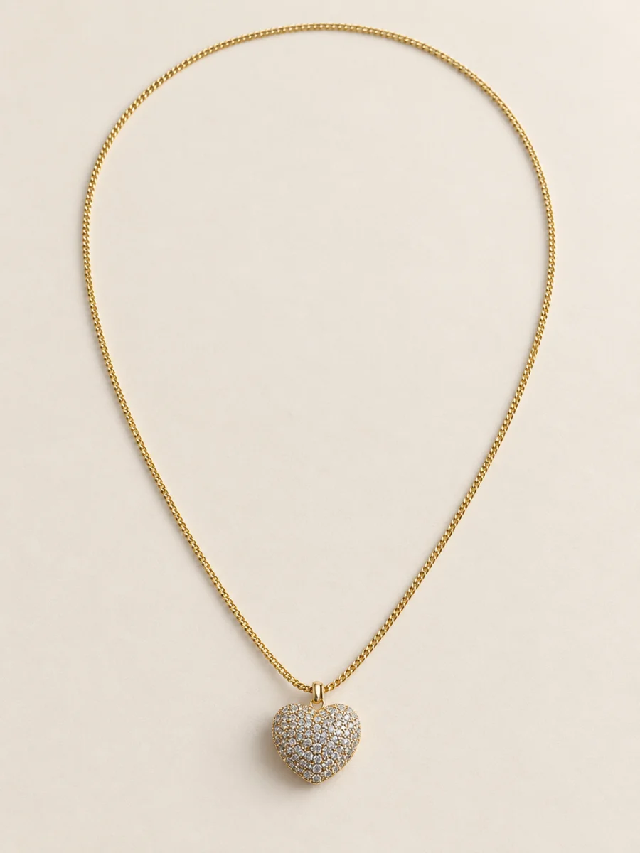 Colar dourado com coração cravejado sobre fundo bege