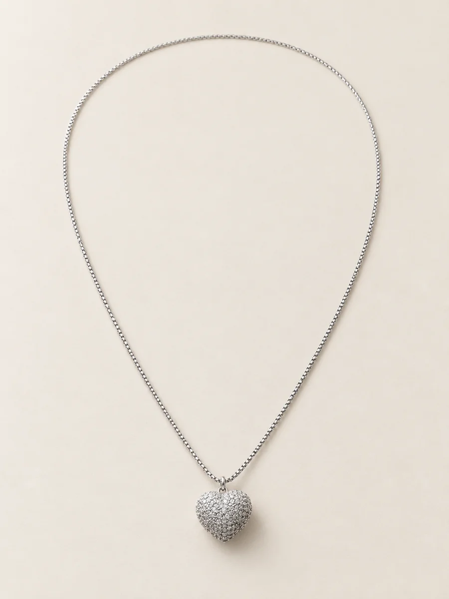 Colar em ouro branco com coração cravejado sobre fundo bege