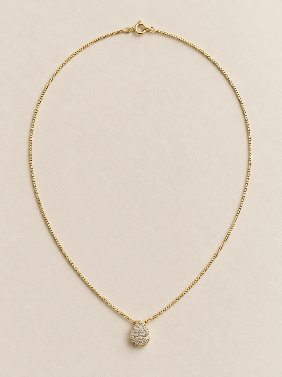 Colar dourado de gota cravejada em fundo bege