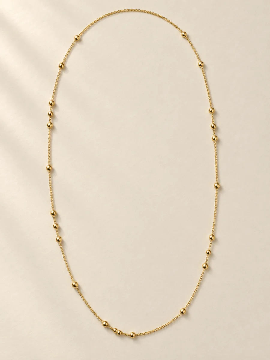 Colar longo dourado com esferas sobre fundo bege