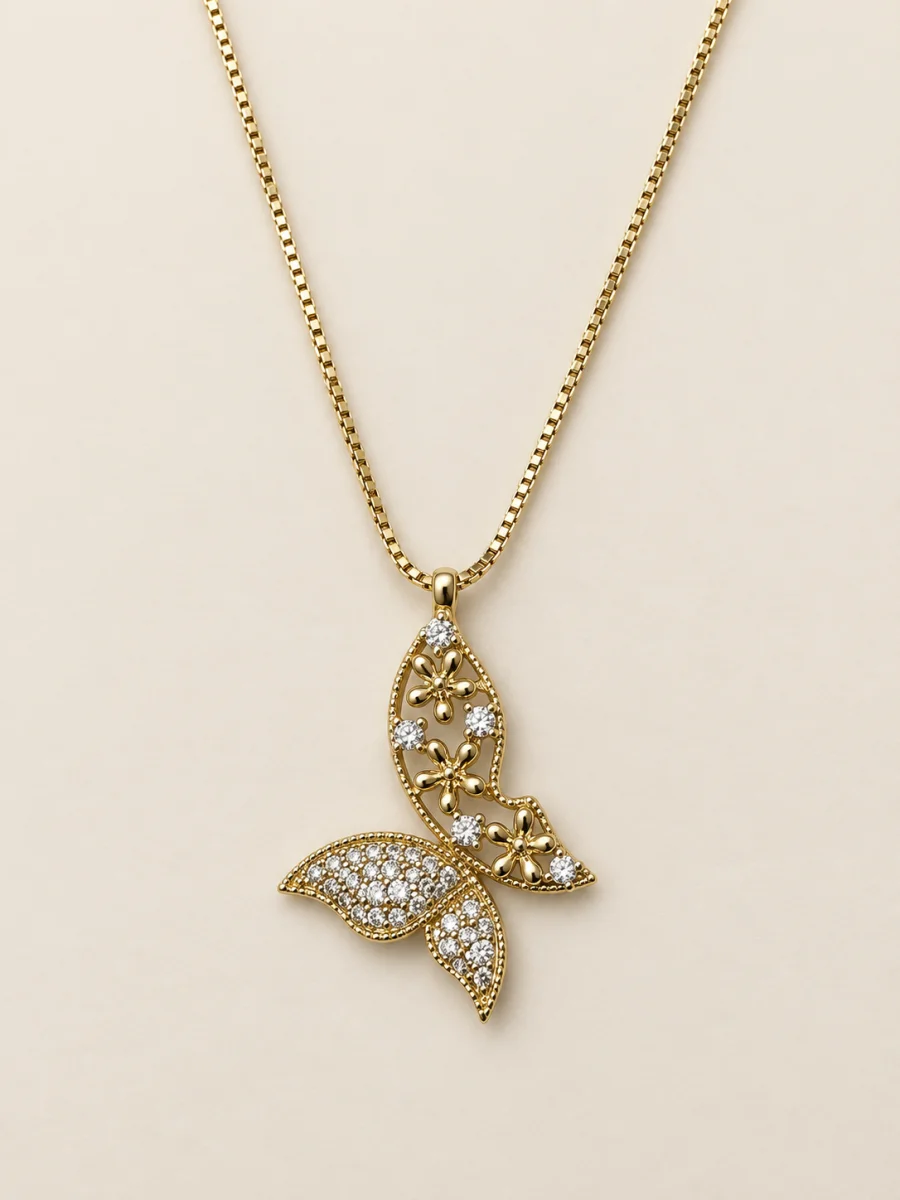 Colar dourado com pingente floral vazado e cauda cravejada sobre fundo bege