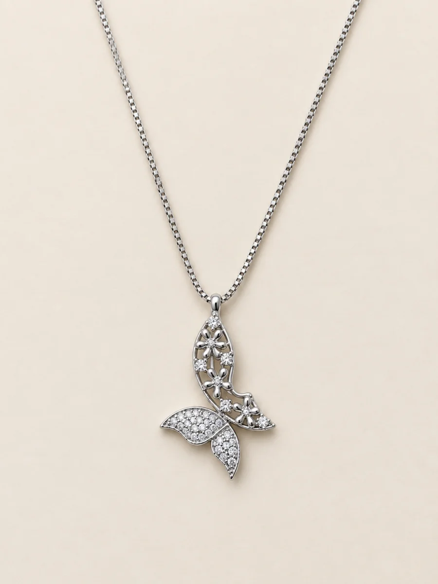 Colar prateado com pingente floral vazado e cauda cravejada sobre fundo bege