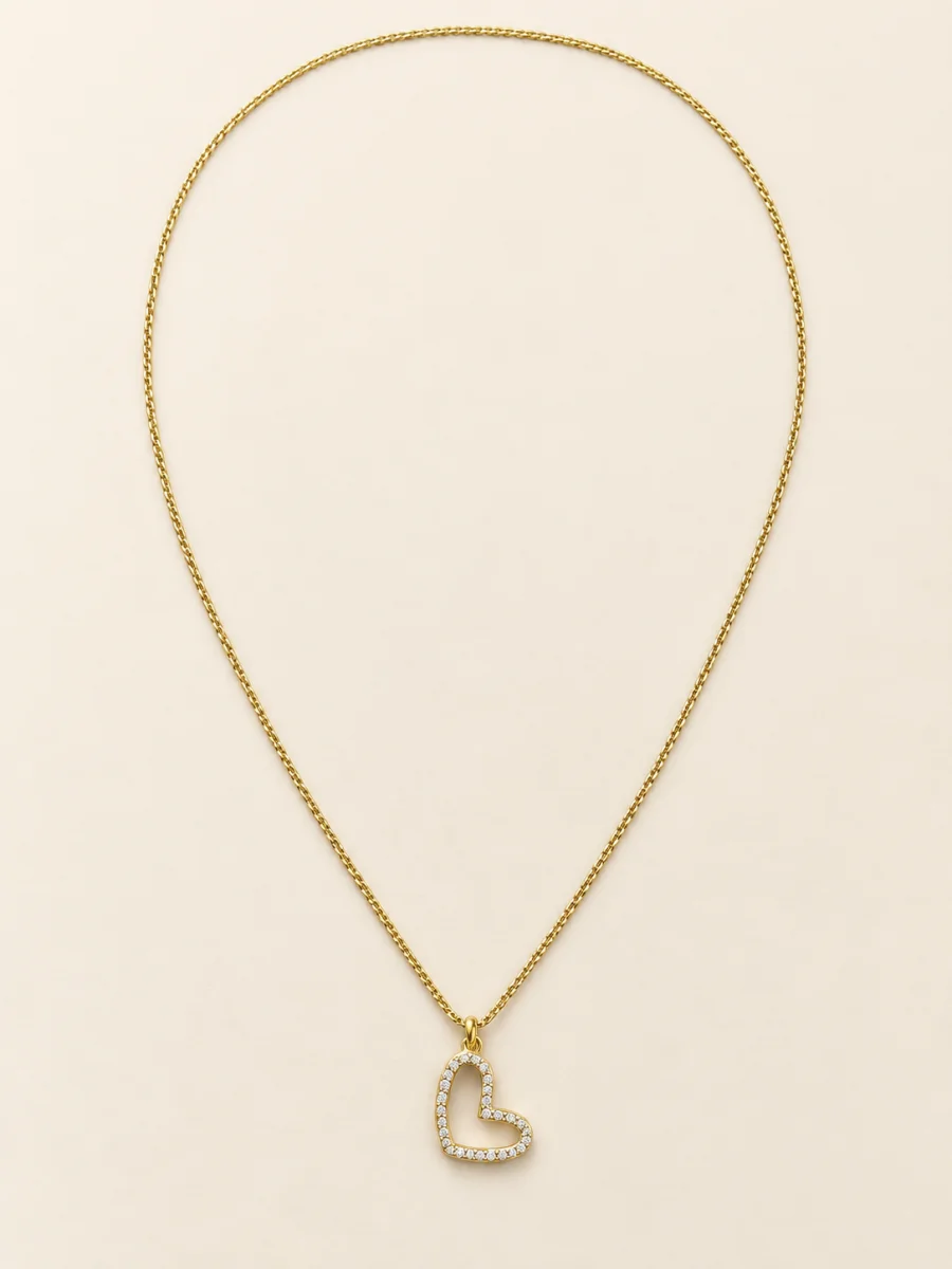 Colar dourado com coração vazado cravejado sobre fundo bege