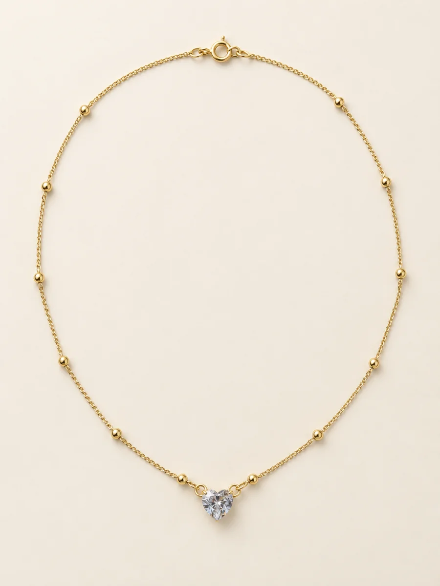 Colar dourado com coração de pedra clara em fundo bege