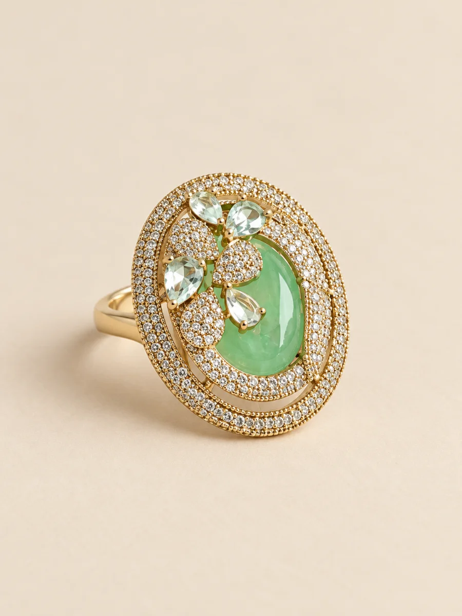 Anel dourado oval com pedra verde sobre fundo bege