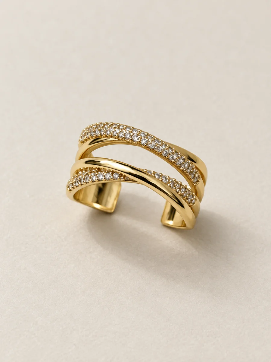 Anel dourado de ondas cruzadas com pedras claras em fundo bege