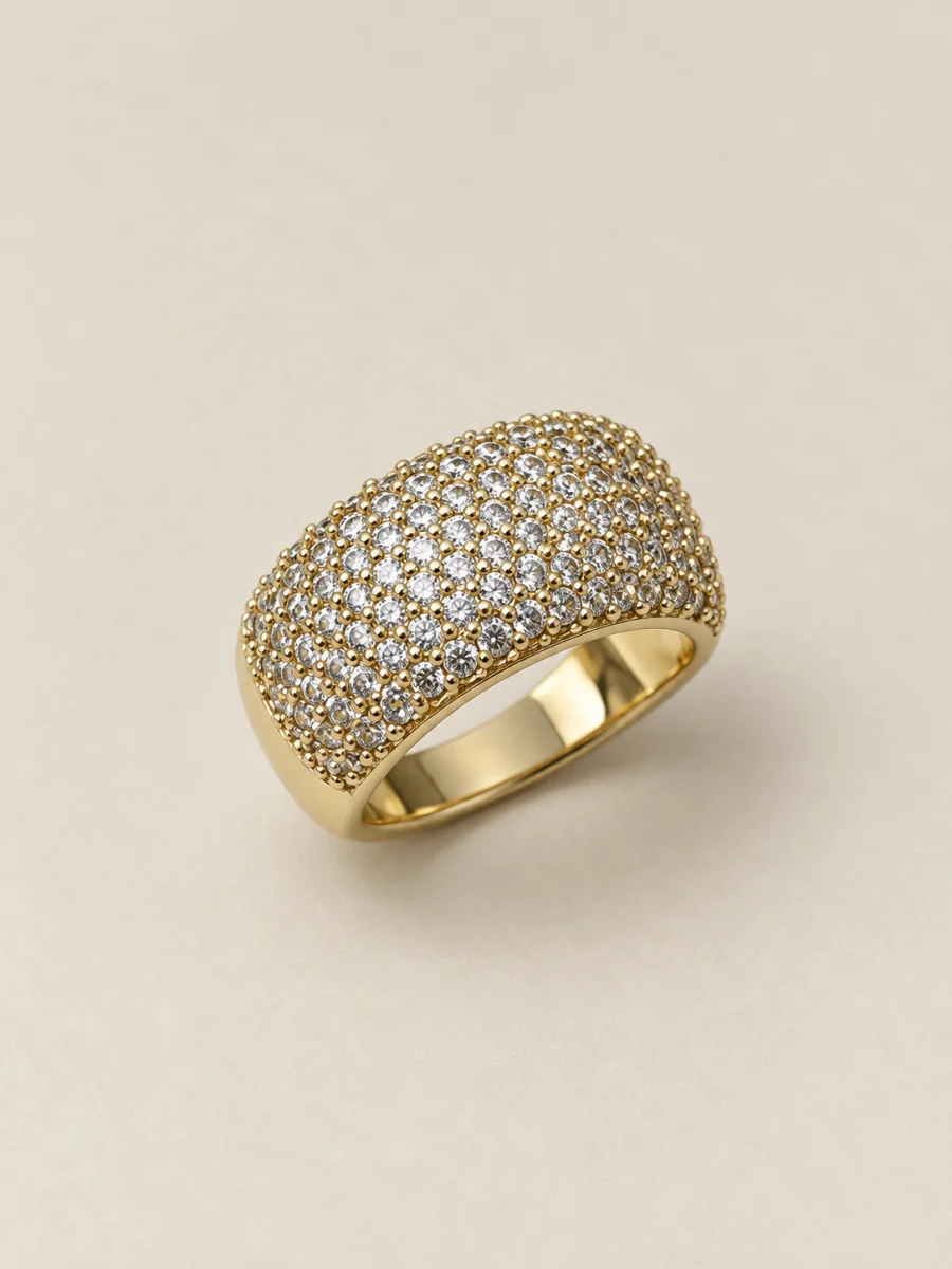 Anel dourado largo com pedras claras cravejadas — fundo bege