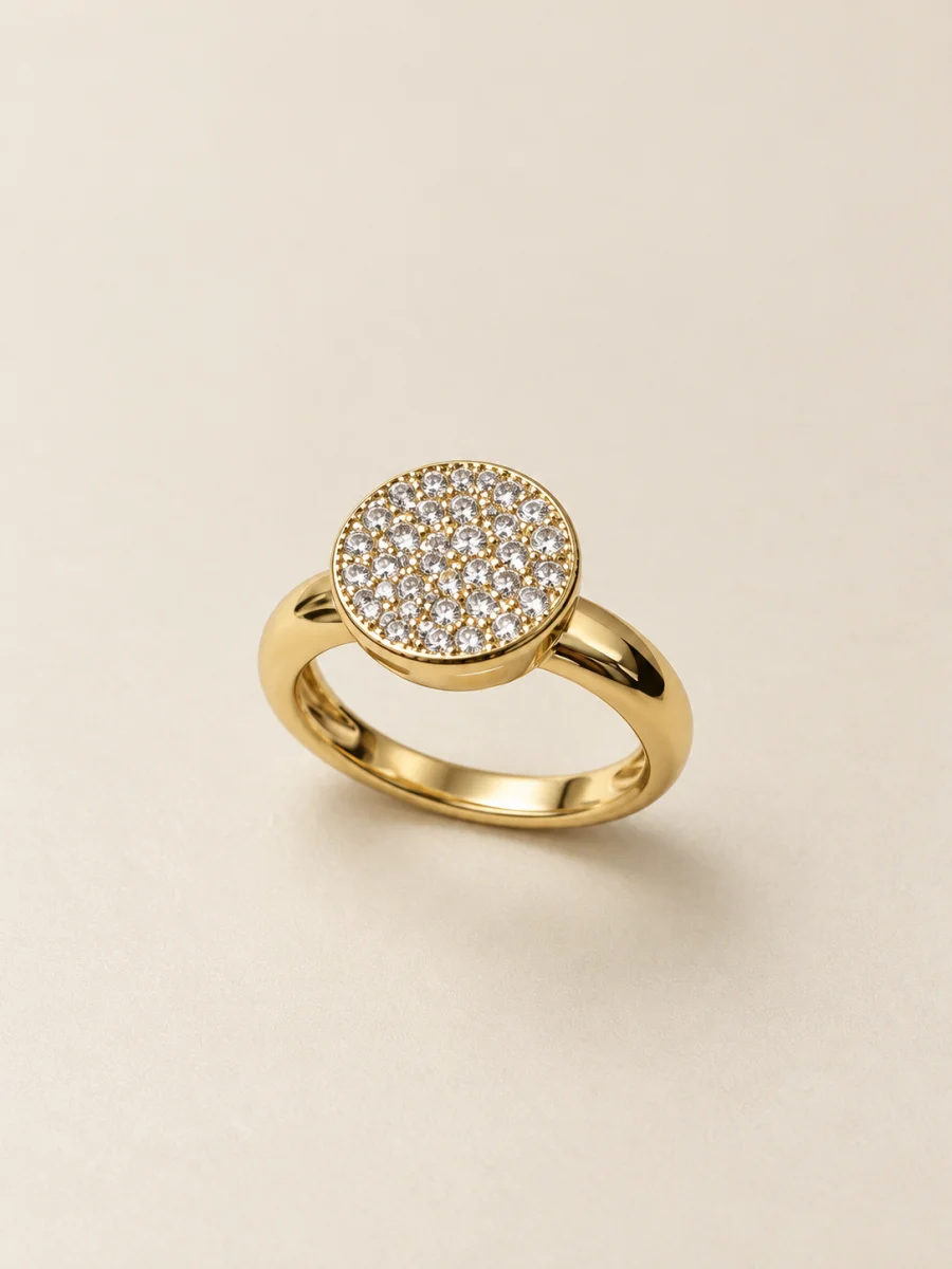 Anel dourado com disco circular cravejado — fundo bege