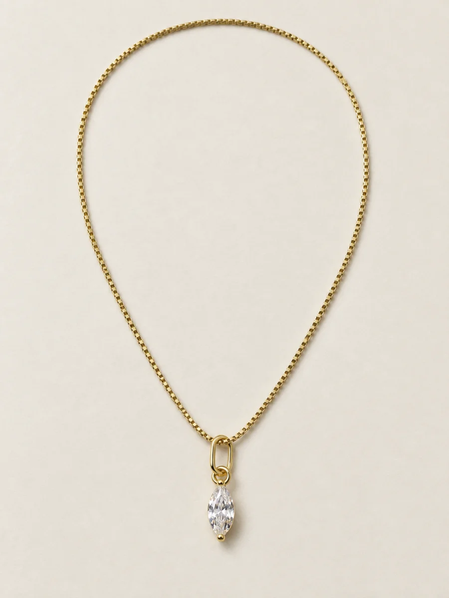 Colar dourado com corrente fina e pingente de gota de pedra clara sobre fundo bege