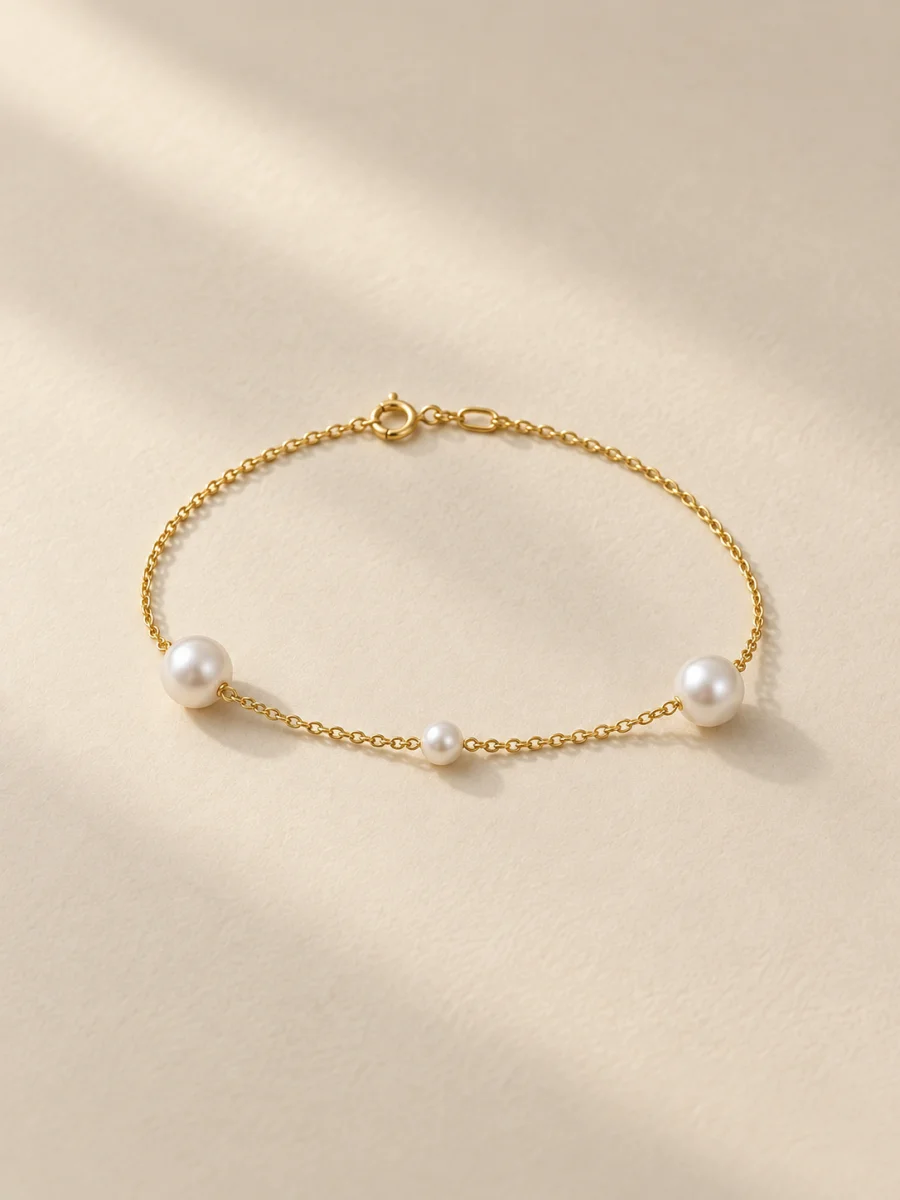 Pulseira dourada de três pérolas sobre fundo bege · formato 3:4