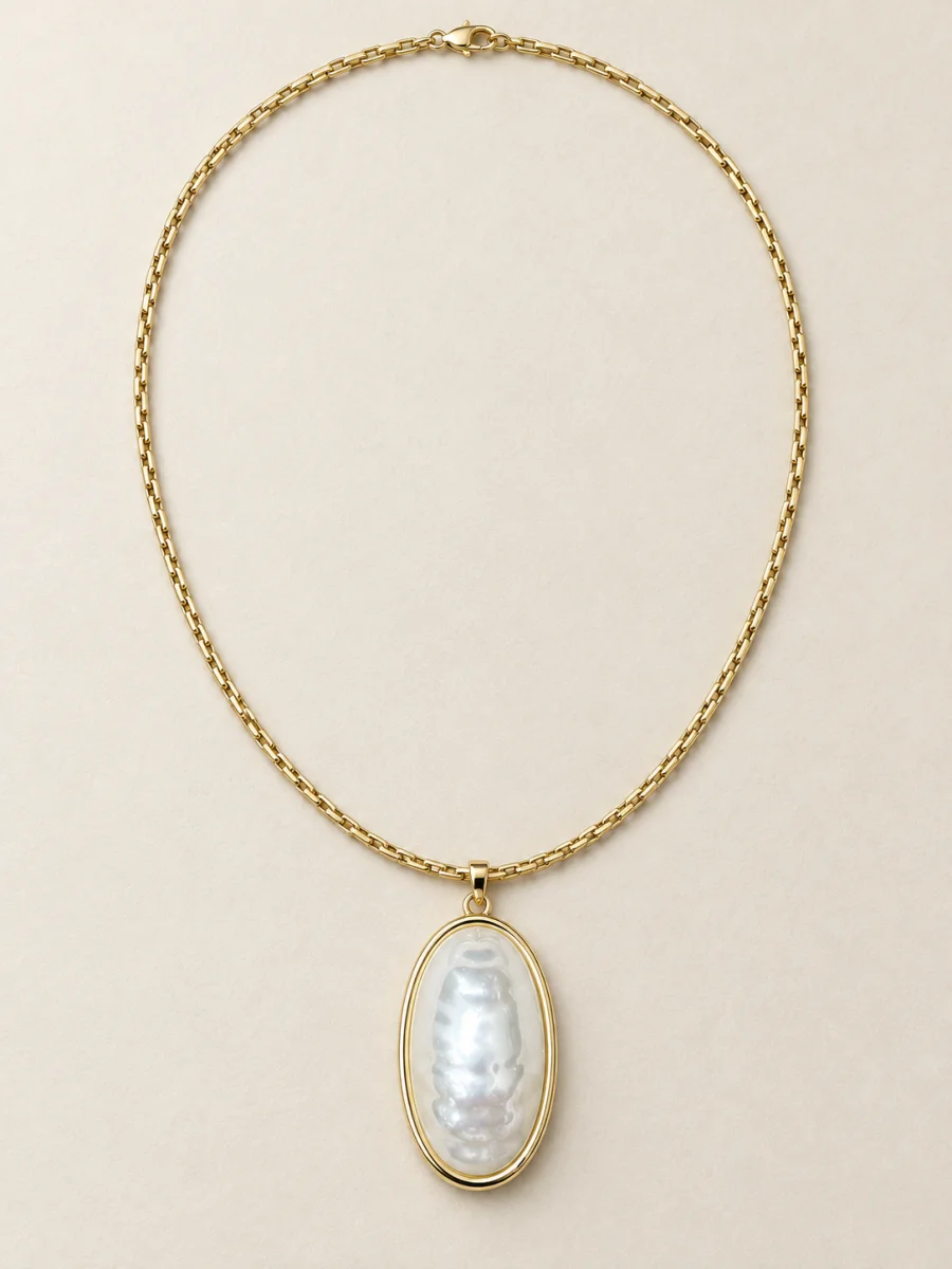 Colar dourado com pingente oval perolado em fundo bege