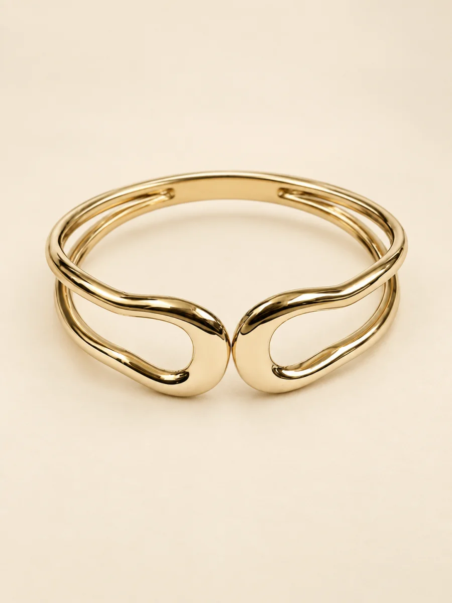 Pulseira dourada de aro ondulado aberto sobre fundo bege claro.