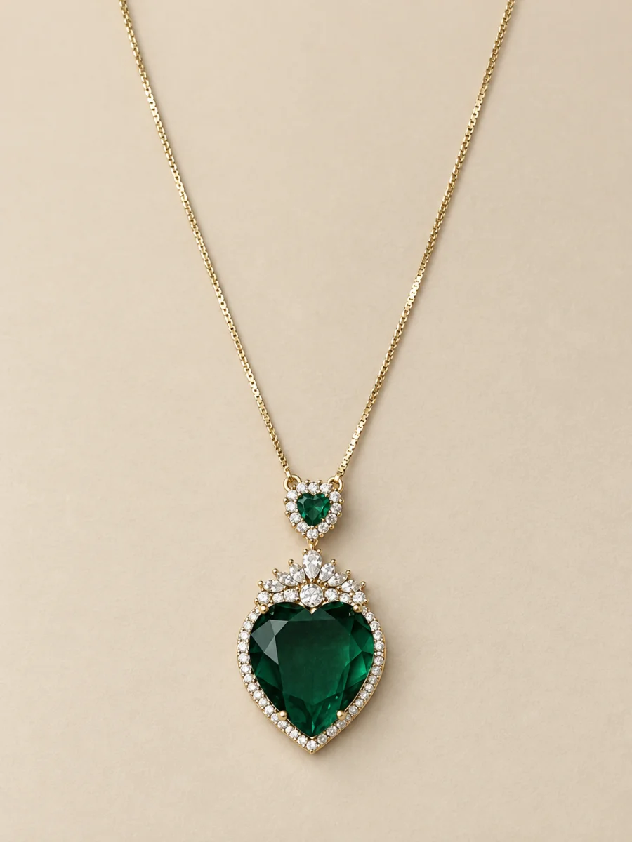 Colar dourado com coração verde cravejado sobre fundo bege