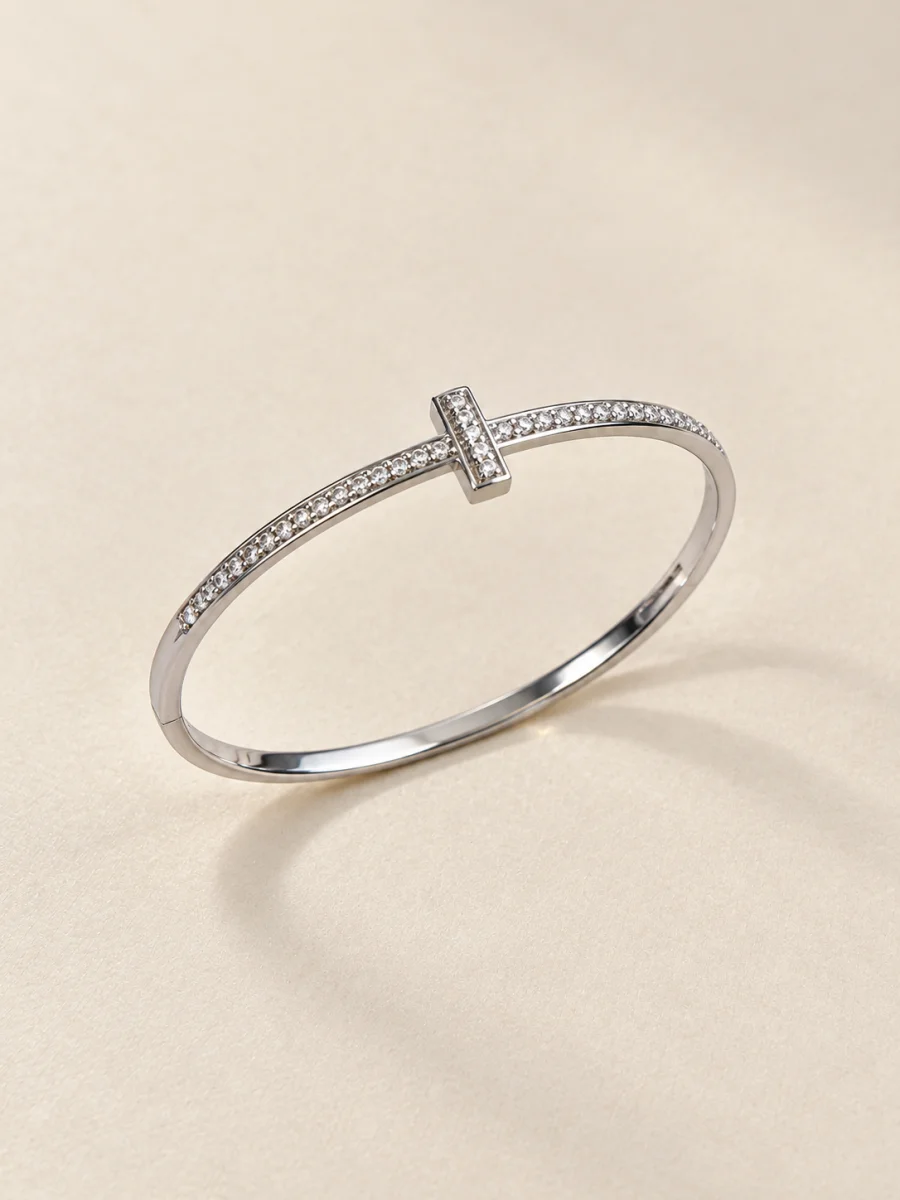 Pulseira prateada com cruz cravejada sobre fundo bege