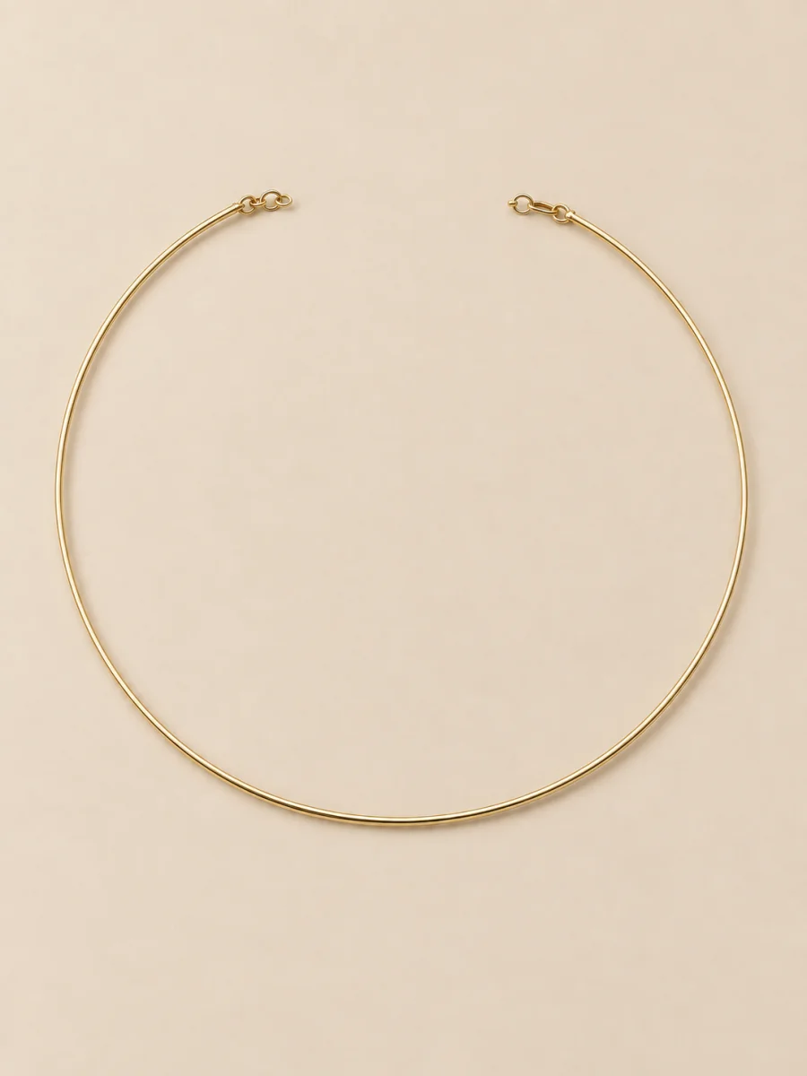 Colar rígido dourado fino e minimalista sobre fundo bege claro.