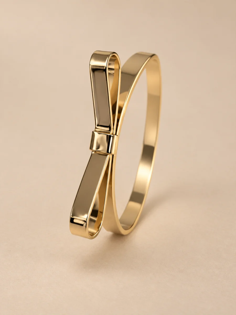 Pulseira dourada com laço escultórico sobre fundo bege