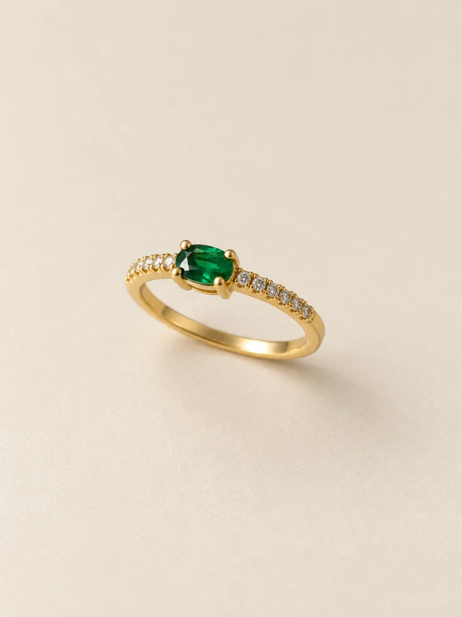 Anel dourado com pedra verde oval e pedras claras nas laterais, em fundo bege