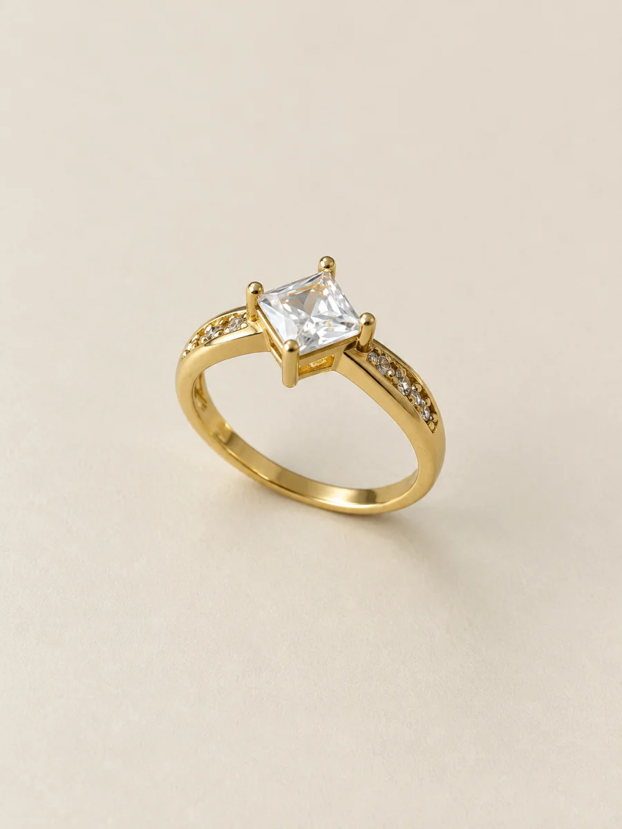 Anel dourado com pedra quadrada clara sobre fundo bege