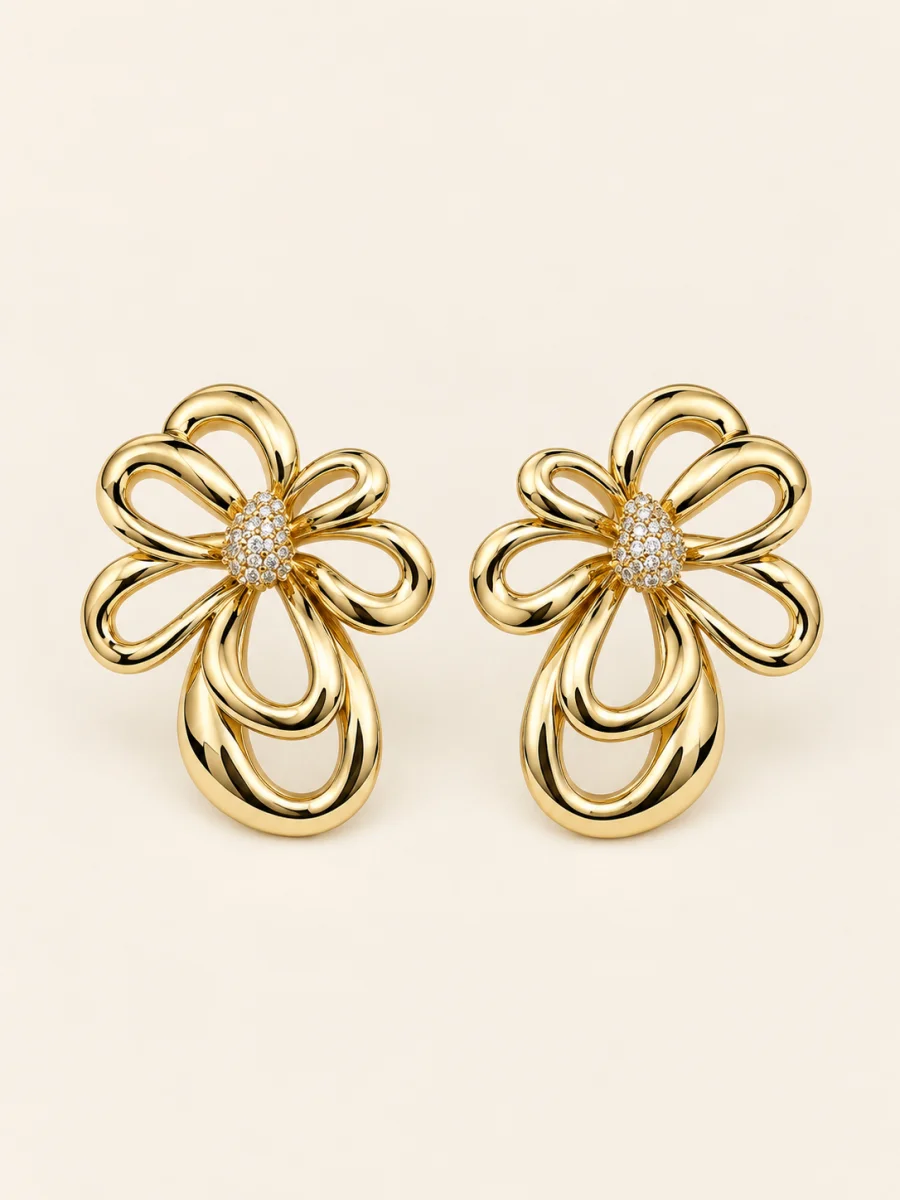 Brinco floral dourado vazado com centro cravejado em fundo bege.
