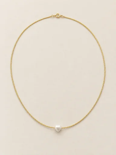 Colar dourado com pérola em coração sobre fundo bege