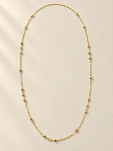 Colar longo dourado com esferas sobre fundo bege