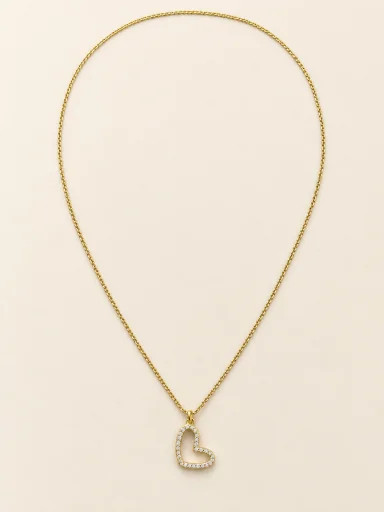 Colar dourado com coração vazado cravejado sobre fundo bege
