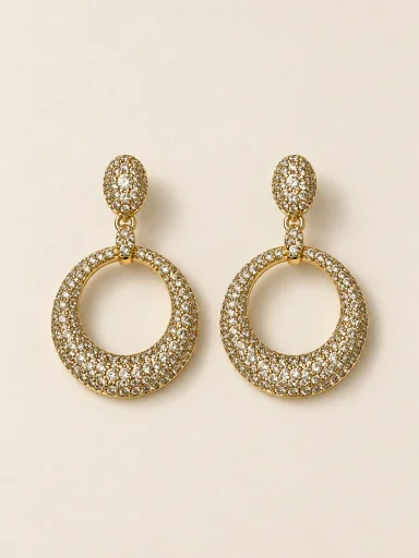 Par de brincos dourados com base oval e argola circular cravejada sobre fundo bege