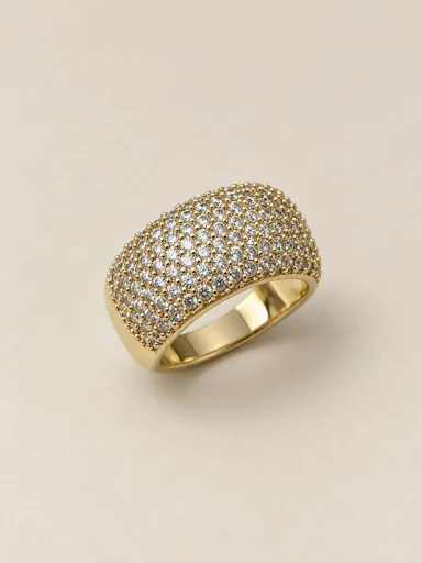 Anel dourado largo com pedras claras cravejadas — fundo bege