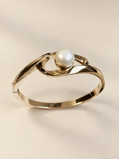 Pulseira dourada de aro com pérola sobre fundo bege