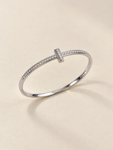 Pulseira prateada com cruz cravejada sobre fundo bege