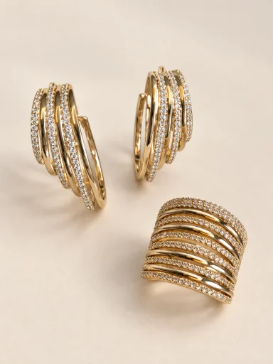 Conjunto de brincos e anel dourados com faixas cravejadas em fundo bege