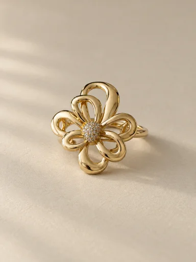 Anel floral dourado com centro cravejado sobre fundo bege