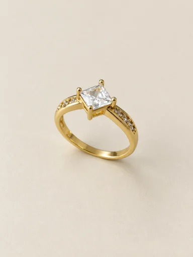 Anel dourado com pedra quadrada clara sobre fundo bege
