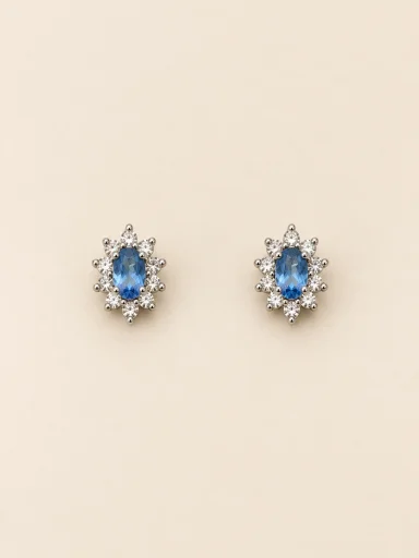 Par de brincos prateados florais com pedra azul oval e detalhes claros, em fundo bege.